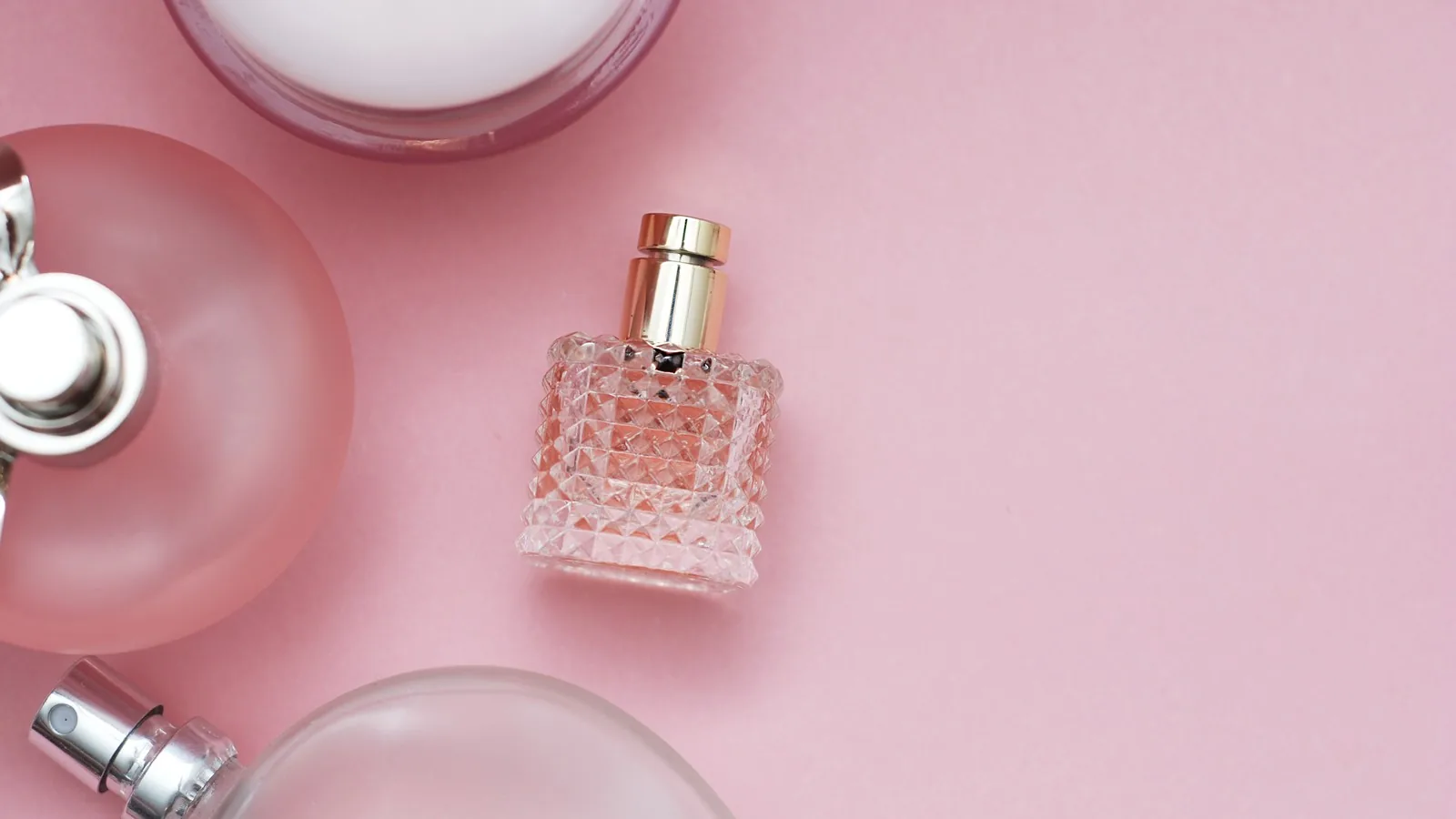 A close overhead view of several unbranded frosted and cut glass perfume bottles on a pink surface.